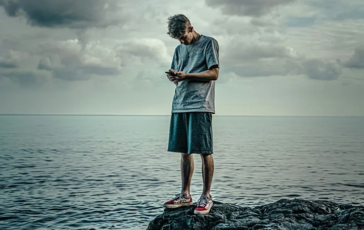 Person standing on rocks by the sea, looking at their phone